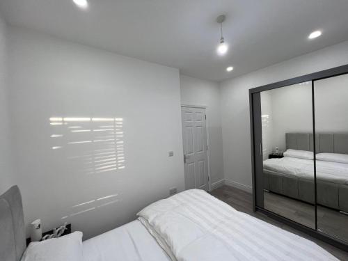 a white bedroom with two beds and a mirror at F3, Luxury Flat close to Ilford. sel in Ilford
