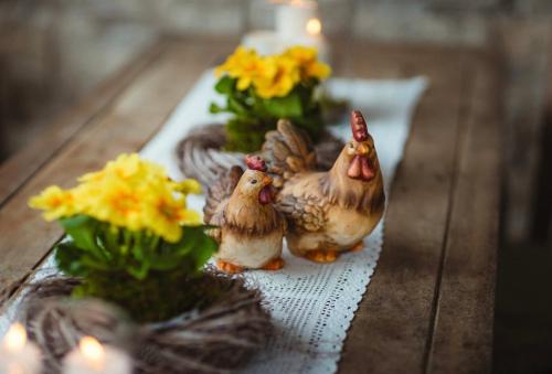 Apartmany pod Pustevnami في بروستريدني بيتشفا: اثنين من تماثيل الدجاج على طاولة مع الزهور
