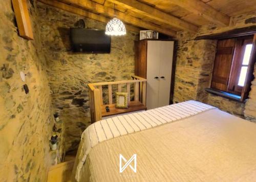 a bedroom with a bed and a tv in a stone wall at MyStay - Casa do Talasnal by Refúgio ao Luar in Talasnal