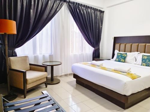 a bedroom with a bed and a chair and a window at Salaam Suites Hotel in Kota Bharu