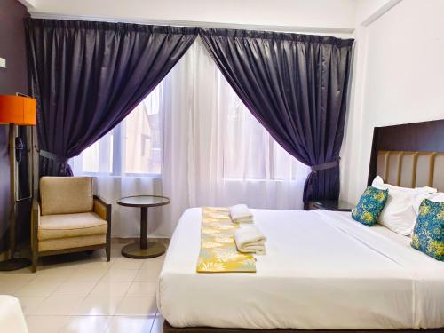 a bedroom with a bed and a chair and a window at Salaam Suites Hotel in Kota Bharu
