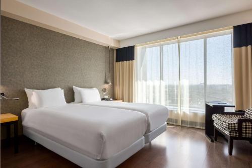 a large white bed in a room with a large window at NH Den Haag in The Hague