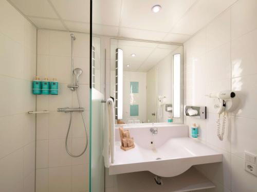 a white bathroom with a sink and a shower at Novotel Maastricht in Maastricht