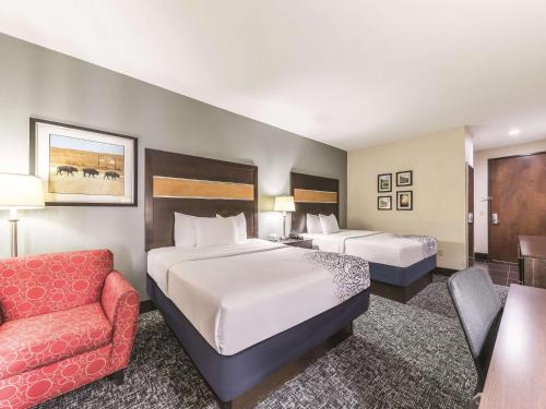 a hotel room with two beds and a chair at La Quinta by Wyndham Tulsa - Catoosa in Catoosa
