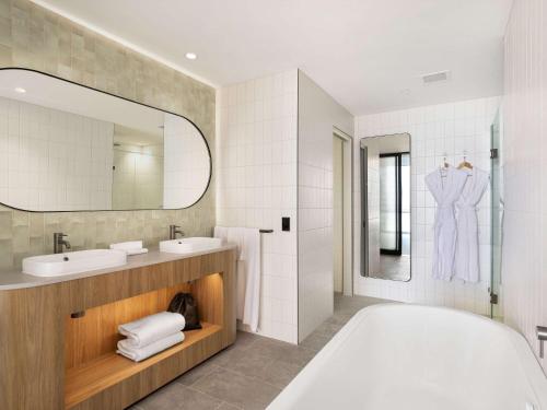 La salle de bains est pourvue d'une baignoire, de 2 lavabos et d'un miroir. dans l'établissement Novotel Surfers Paradise, à Gold Coast