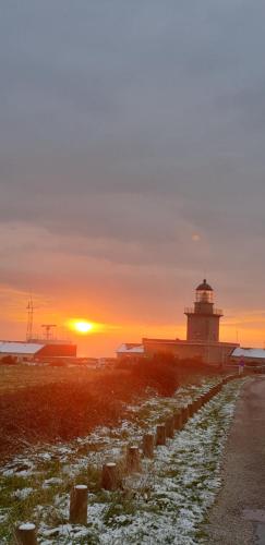 a lighthouse on a beach with the sunset in the background at LE CHALET in Saint-Pierre-dʼArthéglise
