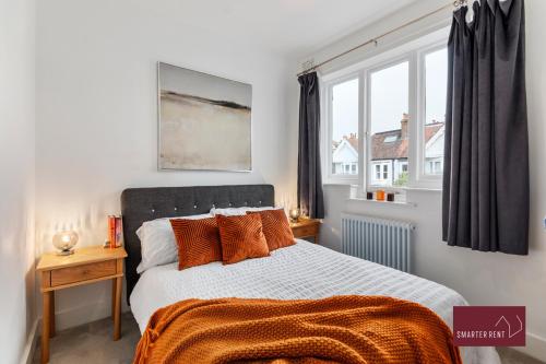a bedroom with a bed with orange pillows and a window at 3 Bedroom Apartment - Kew Village in Richmond upon Thames