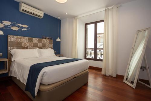 Un dormitorio con una cama con paredes azules y una ventana. en La Casa de la Alameda, en Málaga
