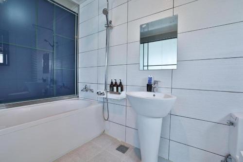 a white bathroom with a sink and a tub and a mirror at Hermes Hotel in Busan