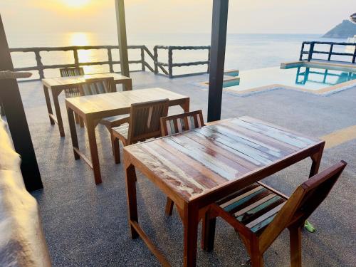 een groep tafels en stoelen met de oceaan op de achtergrond bij Ocean Front Apartments in Ko Tao