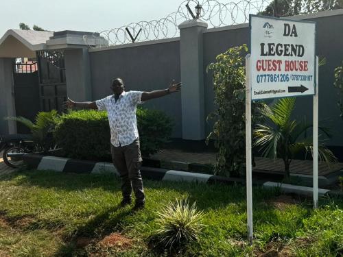a man standing next to a sign in front of a house at DA LEGEND GUEST HOUSE BWEYALE in Kampala