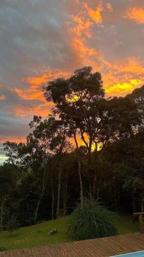 een zonsondergang achter een groep bomen in een veld bij Casa @nomeiodanatureza com piscina e cachoeira in São Francisco Xavier