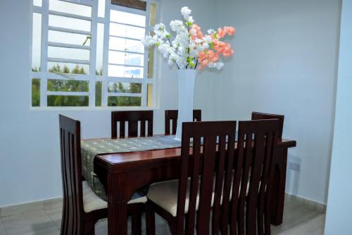 una mesa de comedor y sillas con un jarrón de flores en Meru Heights Luxury Apartments, en Meru