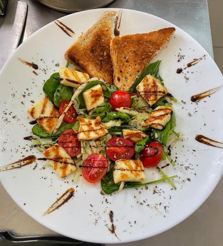 a white plate with a salad with toast and tomatoes at Altus Hotel & Spa in Praid