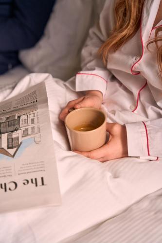 a woman laying in bed with a cup of coffee and a newspaper at The White Horse - A Heartwood Inn in Dorking