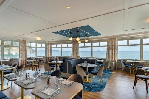 een restaurant met tafels en stoelen en de oceaan bij Hôtel Morgat Le Grand Hôtel De La Mer in Crozon