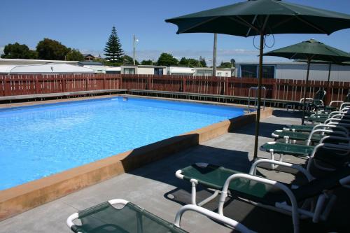 a swimming pool with lawn chairs and an umbrella at Cosy Corner Holiday Park in Mount Maunganui