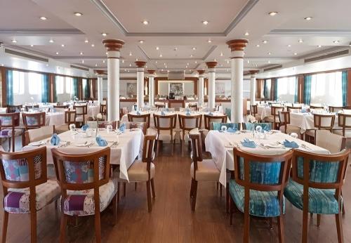 NILE CRUISE LUXOR & ASWAN A في الأقصر: مطعم بطاولات وكراسي في غرفة بها نوافذ