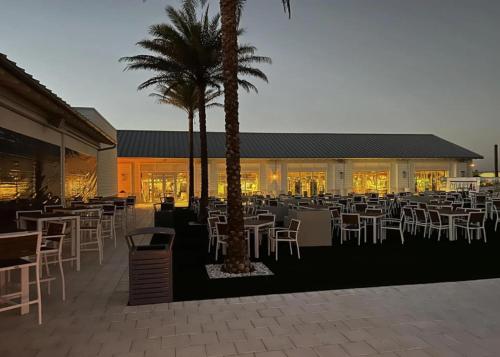 un restaurante con mesas y sillas blancas y palmeras en New Home 3br/25br w/ kayak access sleeps 9, en Orange Beach