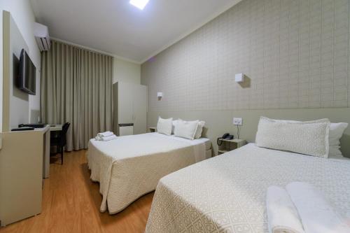 a hotel room with two beds and a desk at Realce Hotel in Jaú