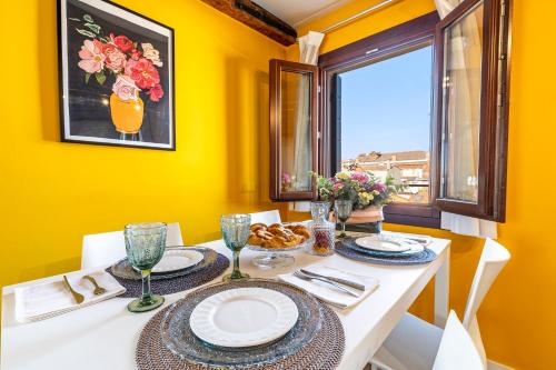 un comedor con paredes amarillas y una mesa con platos y vasos. en Ca' dell'Arciere Apartments, en Venecia