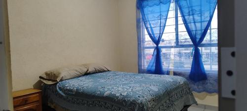 a bedroom with a bed and a window with blue curtains at Casa Latania in El Salto