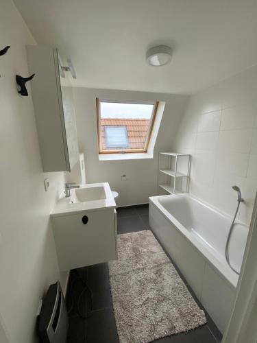 a bathroom with a white tub and a sink and a window at Vakantiehuis De Panne in De Panne
