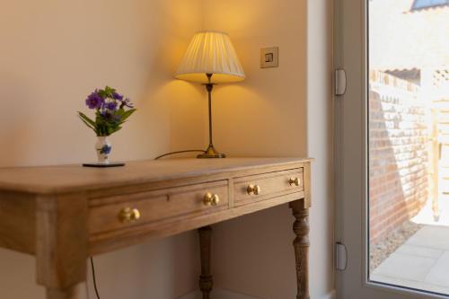 a table with a lamp and a vase of flowers on it at Snipe Meadow Barn by Big Skies Estates in Swafield