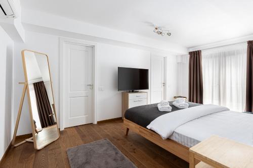 a white bedroom with a bed and a television at PEAK Aparthotel - Old Town - by CityHost in Braşov