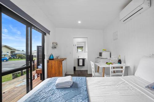 a white bedroom with a bed and a balcony at Joy's Rest Cabin - Whangamata in Whangamata
