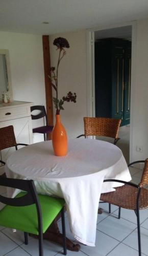 un vase orange assis sur une table blanche avec des chaises dans l'établissement Petite maison de charme, à Langres