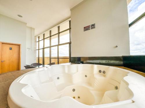 a large white bath tub in a room with windows at Ao lado do Metrô e Shopping (1Qto) in Brasilia