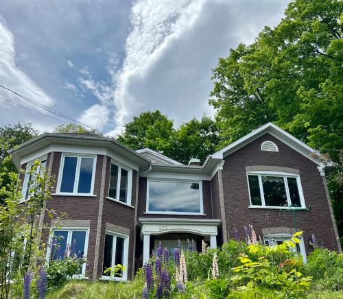a brick house with purple flowers in the yard at Newly Renovated villa with magnificent views in Coaticook