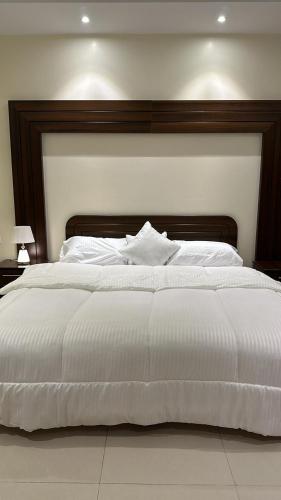 ein großes weißes Bett mit einem Kopfteil aus Holz in der Unterkunft شقة مفروشة بدخول ذاتي in Al Kharj