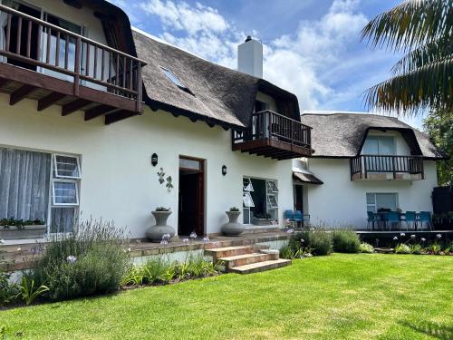a white house with a thatched roof and a yard at Tree Aloe Guest house in St Francis Bay