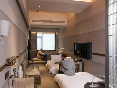 uma pessoa sentada num quarto de hotel com duas camas em NOA Hotel & SPA Shenzhen em Shenzhen
