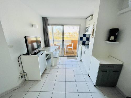 Il comprend une cuisine dotée de carrelage blanc, d'une table et d'une télévision. dans l'établissement Appartement avec Piscine, Climatisation, et Parking à 2 Pas de la Plage - FR-1-723-133, au Cap d'Agde