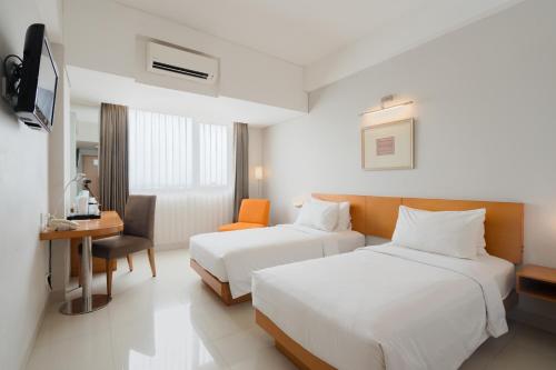 a hotel room with two beds and a desk at The Capital Hotel Surabaya in Surabaya