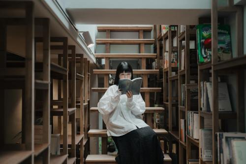 a woman standing in a library reading a book at Norden Ruder Hostel Taitung Branch 2 in Taitung City