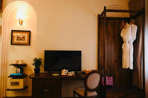 Zimmer mit einem Schreibtisch, einem TV und einem an einem Schrank hängenden Kleid. in der Unterkunft La Belle Maison in Hanoi