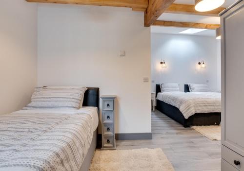 two beds in a room with white walls and wooden ceilings at The Barn at the Grange in Hawes