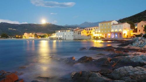 uma cidade na costa de um corpo de água à noite em Studio standing classé avec terrasse vue mer " les pieds dans l'eau " à Algajola em Algajola