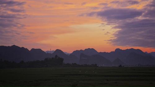 una puesta de sol sobre un campo con montañas en el fondo en Palafita Bungalow, en Phong Nha