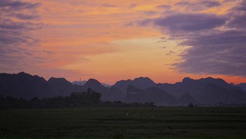 a sunset over a field with mountains in the background at Palafita Bungalow in Phong Nha