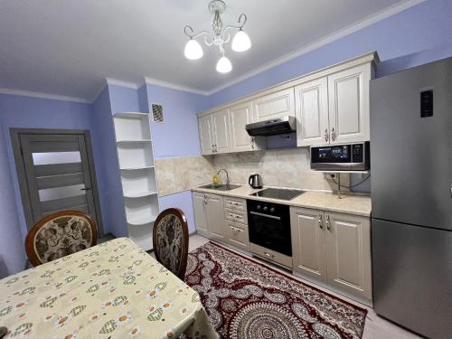 een keuken met witte kasten, een tafel en een koelkast bij Апартаменты напротив спорткомплекса Алматы Арена 81-29 in Alma-Ata