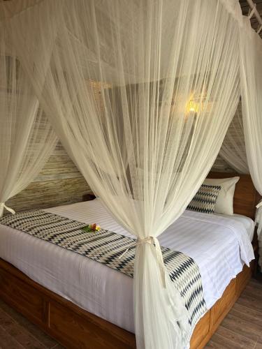 a bedroom with a canopy bed with white curtains at 221 Garden Cottages in Nusa Lembongan