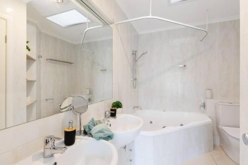 uma casa de banho branca com uma banheira e um lavatório e uma banheira em Spacious 2 Bed/2 Bath Garden Apartment Aircon em Brisbane