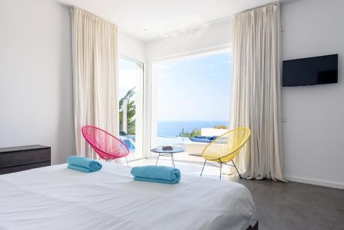 a bedroom with a bed with two chairs and a large window at Villa Nineten in Roca Llisa