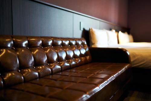 a brown leather couch in a hotel room with a bed at Rakuten STAY Kokura Station in Kitakyushu