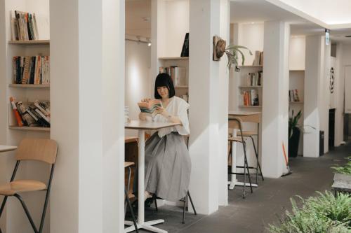 a woman sitting at a table reading a book at Norden Ruder Hostel Taitung in Taitung City